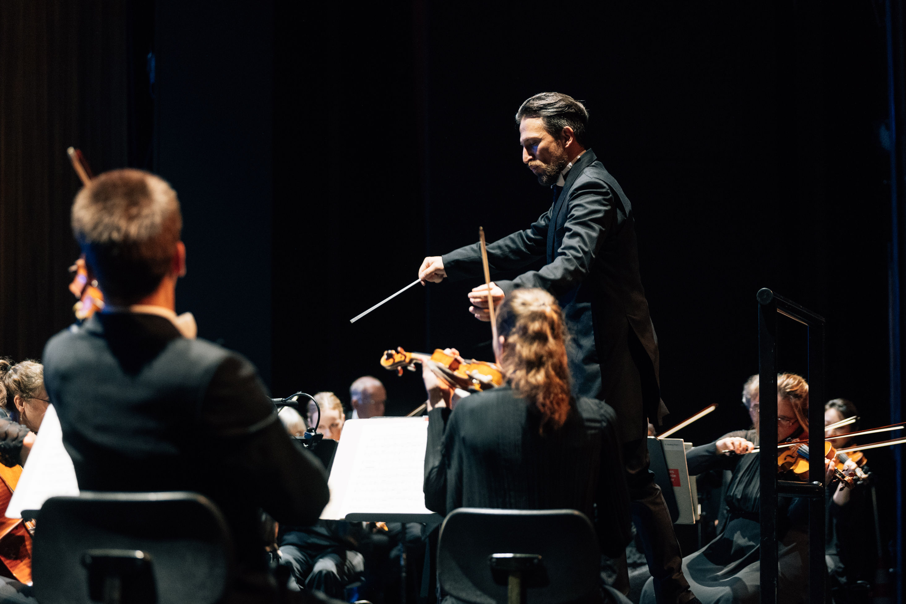 Cornelius Meister steht am Dirigentenpult und dirigiert das Orchester.