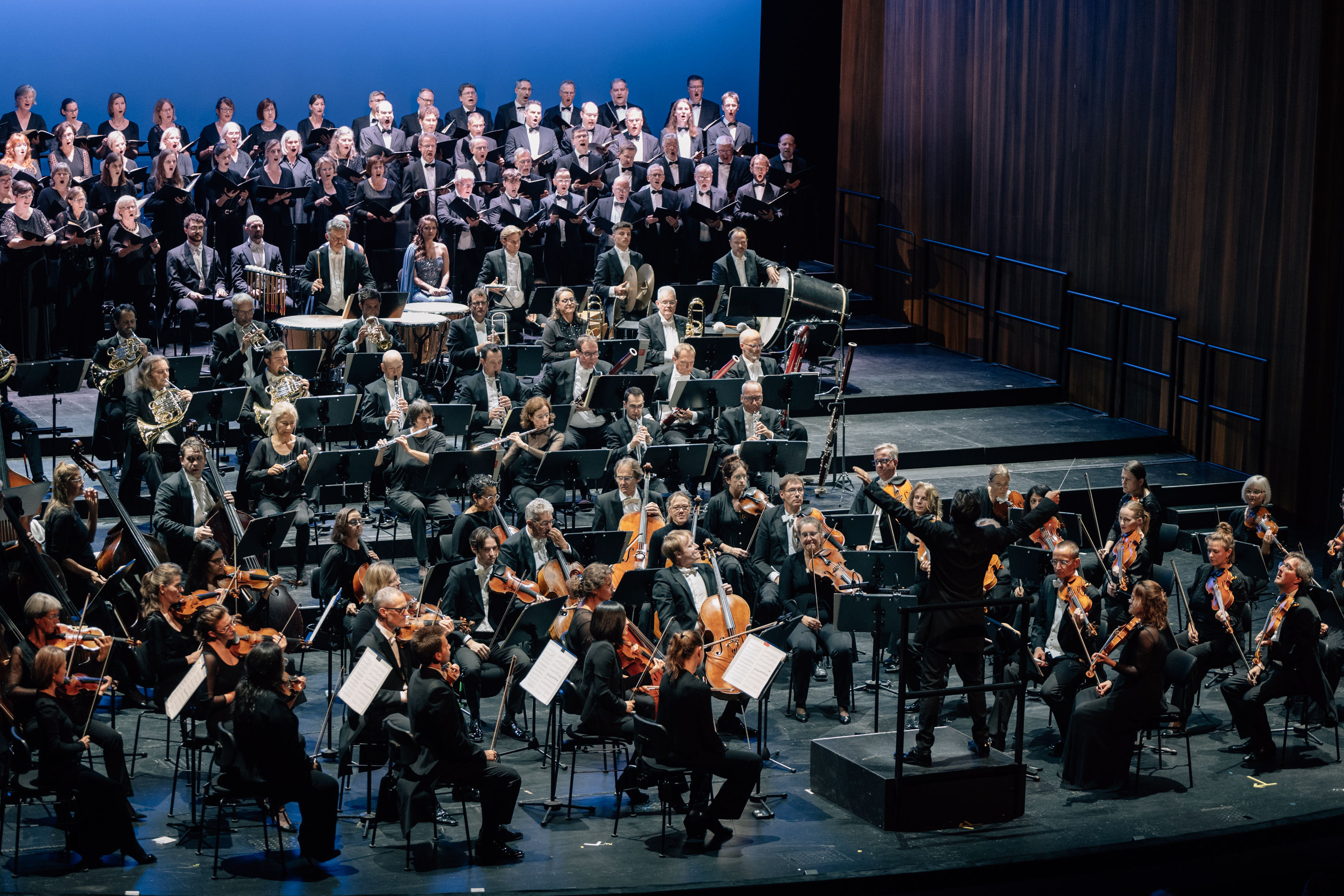 Blick auf die Bühne der Oper Bonn mit dem Orchester und dem Chor. Vor dem Chor sitzen die Solist:innen.