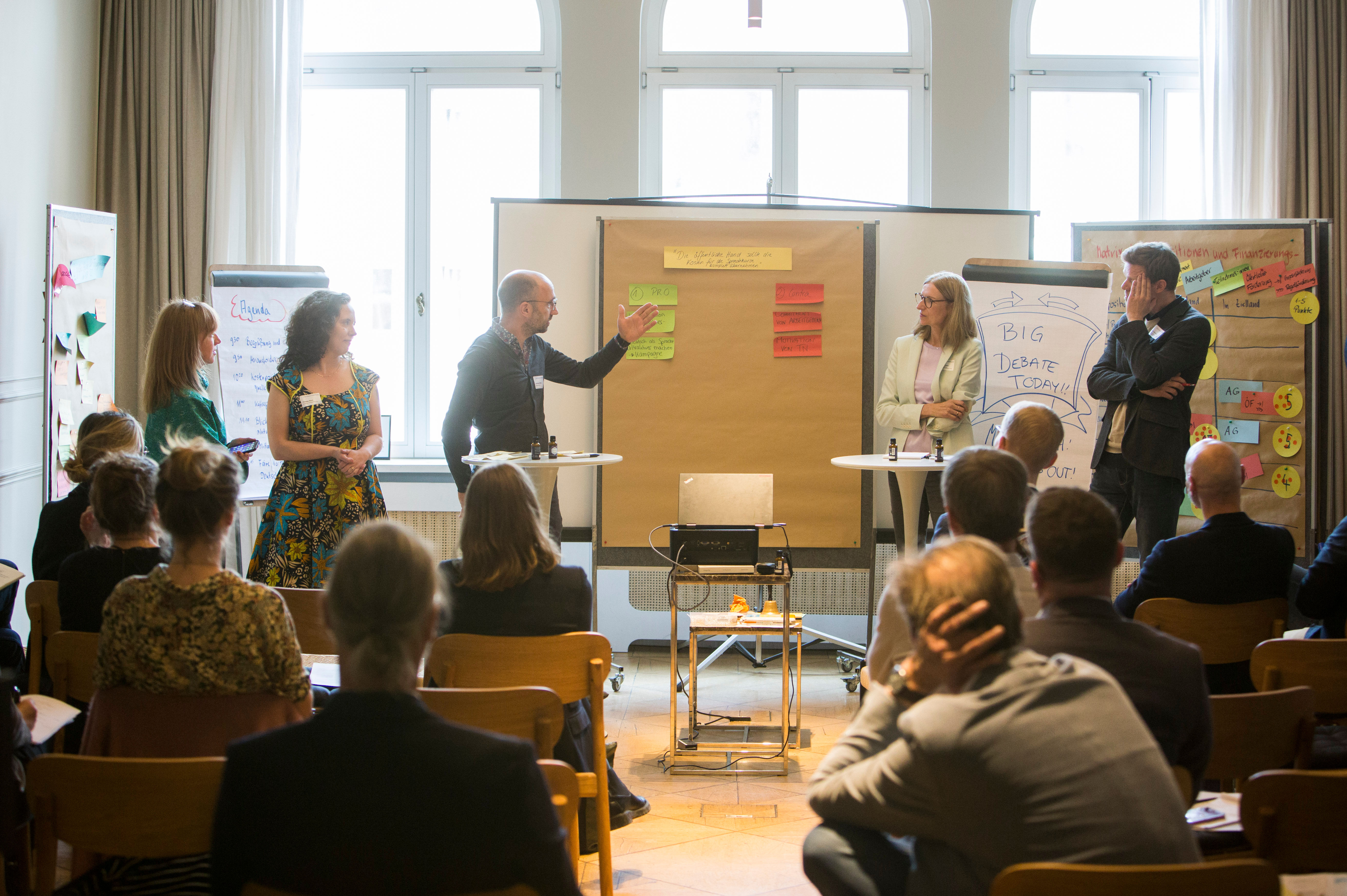 fünf Teilnehmende am Workshop der Denkfabrik stehen um eine Metaplanwand mit Moderationskärtchen herum und präsentieren etwas